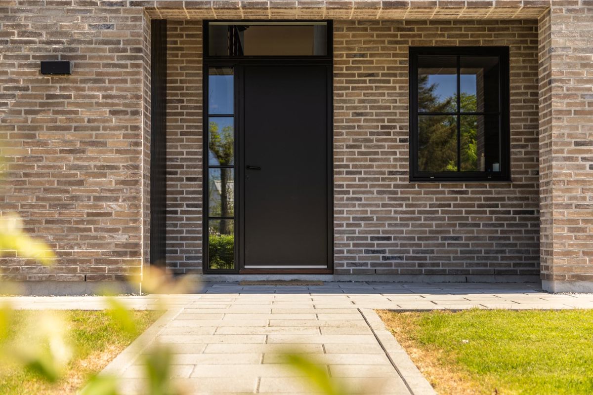 Nybyggeri med lyse mursten og sort pladedør med sideparti med sprosser og overparti, i klart glas, med tilhørende vindue dertil Nybyggeri med lyse mursten og sort pladedør med sideparti med sprosser og overparti, i klart glas, med tilhørende vindue dertil